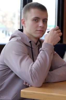 Yol kenarındaki bir kafede kahve içen yakışıklı bir genç.