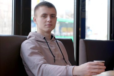 Yol kenarındaki bir kafede kahve içen yakışıklı bir genç.