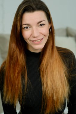 Uzun kızıl saçlı, siyah gömlekli, stüdyoda yatağın üzerinde poz veren genç bir kız.