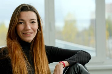 Uzun kızıl saçlı, siyah gömlekli, stüdyoda yatağın üzerinde poz veren genç bir kız.