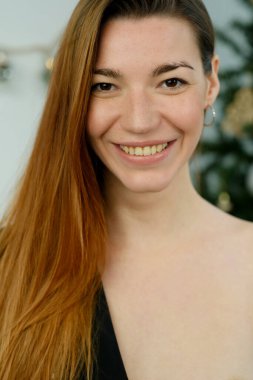 Uzun kızıl saçlı, siyah gömlekli, stüdyoda yatağın üzerinde poz veren genç bir kız.