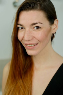 Uzun kızıl saçlı, siyah gömlekli, stüdyoda yatağın üzerinde poz veren genç bir kız.