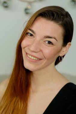 Uzun kızıl saçlı, siyah gömlekli, stüdyoda yatağın üzerinde poz veren genç bir kız.