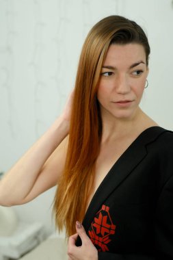 Uzun kızıl saçlı, siyah gömlekli, stüdyoda yatağın üzerinde poz veren genç bir kız.