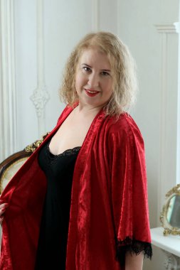 Yaşlı, güzel, sarışın, kırmızı cüppeli kıvırcık bir kadın stüdyoda poz veriyor..