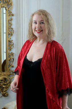 Yaşlı, güzel, sarışın, kırmızı cüppeli kıvırcık bir kadın stüdyoda poz veriyor..