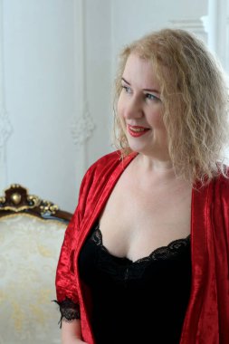 Yaşlı, güzel, sarışın, kırmızı cüppeli kıvırcık bir kadın stüdyoda poz veriyor..