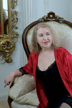 Yaşlı, güzel, sarışın, kırmızı cüppeli kıvırcık bir kadın stüdyoda poz veriyor..