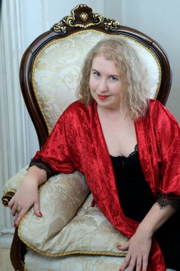 Yaşlı, güzel, sarışın, kırmızı cüppeli kıvırcık bir kadın stüdyoda poz veriyor..