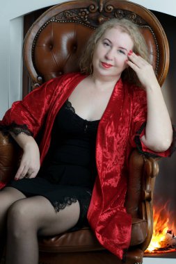 Yaşlı, güzel, sarışın, kırmızı cüppeli kıvırcık bir kadın stüdyoda poz veriyor..