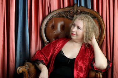 Yaşlı, güzel, sarışın, kırmızı cüppeli kıvırcık bir kadın stüdyoda poz veriyor..