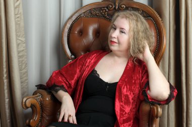 Yaşlı, güzel, sarışın, kırmızı cüppeli kıvırcık bir kadın stüdyoda poz veriyor..