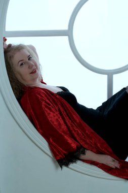 Yaşlı, güzel, sarışın, kırmızı cüppeli kıvırcık bir kadın stüdyoda poz veriyor..