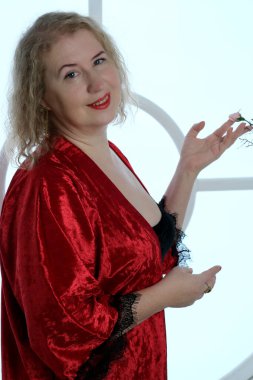 Yaşlı, güzel, sarışın, kırmızı cüppeli kıvırcık bir kadın stüdyoda poz veriyor..