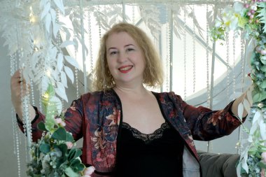 Yaşlı, güzel, sarışın, kıvırcık saçlı, kırmızı cüppeli bir kadın stüdyoda poz veriyor.