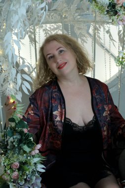 Yaşlı, güzel, sarışın, kırmızı cüppeli kıvırcık bir kadın stüdyoda poz veriyor..