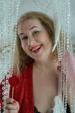 Yaşlı, güzel, sarışın, kırmızı cüppeli kıvırcık bir kadın stüdyoda poz veriyor..