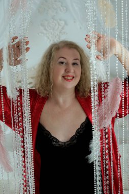 Yaşlı, güzel, sarışın, kırmızı cüppeli kıvırcık bir kadın stüdyoda poz veriyor..