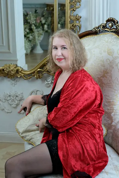 Yaşlı, güzel, sarışın, kırmızı cüppeli kıvırcık bir kadın stüdyoda poz veriyor..