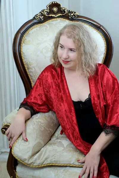 Yaşlı, güzel, sarışın, kırmızı cüppeli kıvırcık bir kadın stüdyoda poz veriyor..