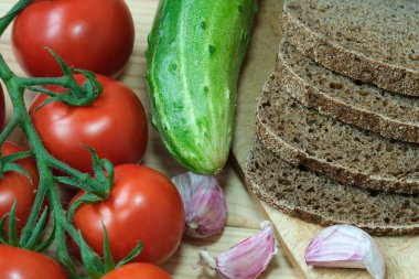 Bir yığın ekmek bir yığın domates ve bir salatalığın yanında oturur..