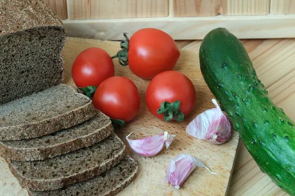 Üstünde ekmek, domates ve salatalık dilimleri olan tahta bir tahta kesme tahtası..