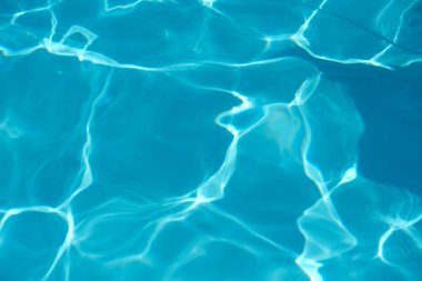 Yüzeyden yansıyan ışıkla birlikte mavi havuz suyunun yakın çekim görüntüsü dalgalanmalar yaratıyor..