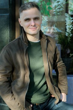 Neşeli adam açık havada canlı bir çiçek aranjmanının yanında poz veriyor..