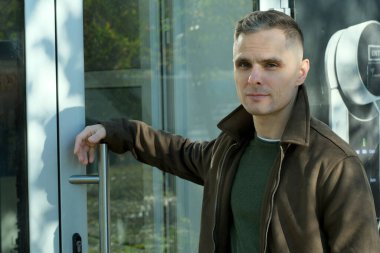 Kendine güveni olan bir birey şık cam bir kapının yanında duruyor, şehir modasını ve cazibesini sergiliyor..