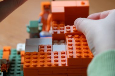 Eller neşeli bir inşaatta canlı turuncu tuğlaları nazikçe istifler..