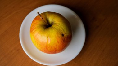 Sarı ve kırmızı tonları olan canlı bir elma bir tabakta oturur..
