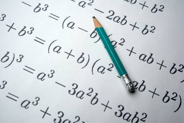 Değişkenlerle dolu matematiksel denklemler yeşil bir kalemin altında yatıyor.