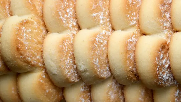 Taze pişmiş tatlı börekler yakın planda oturur, yumuşak, altın kabuklarını sergilerler. Narin tabakalar hafif şekerle kaplanmış, sıcak ve rahatlatıcı bir his uyandırıyor..