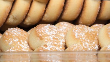 Sıcak, pudra şekerli altın kurabiyeler temiz bir kapta güzelce istiflenir. Fırınlanmış malların davetkar kokusu havayı dolduruyor, ziyaretçiler için hoş bir ikram vaat ediyor..