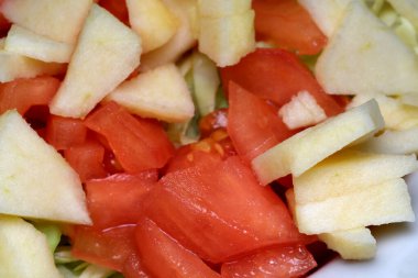 Parlak kırmızı domatesler ve çıtır çıtır yeşil elmaların enfes bir karışımı kaseyi doldurarak salatanın tazeliğini gözler önüne seriyor. Güneş ışığı renkleri güçlendirir, ferahlatıcı bir tat yaratır..