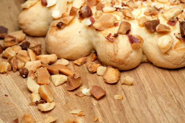 Sıcak ahşap bir yüzeye serpiştirilmiş fındık serpiştirilmiş taze pişmiş hamur işi. Lezzetli aroma ve doku hoş bir mutfak deneyimini davet ediyor..