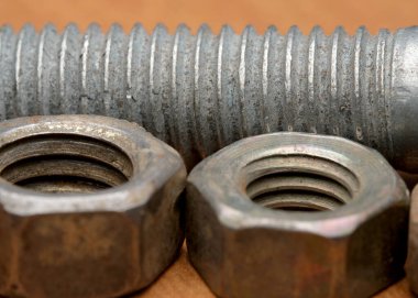 Metalik fındık ve cıvataların yakın çekim görüntüsü ahşap bir arka planda duruyor..