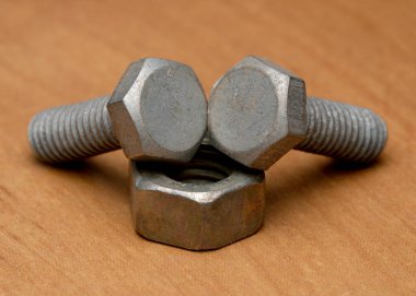 Üç metalik cıvata ve bir fındık ahşap bir arka planda yaratıcı bir şekilde sergilenir..