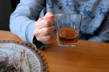 Tahta bir masada oturmuş, dinlenirken bir bardak çay içen bir insan..