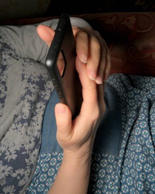 Bir insan rahat bir şekilde uzanır, gece geç saatlerde akıllı telefonuyla meşgul olur..