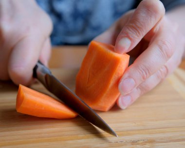 Yetenekli eller ahşap bir tahtanın üzerinde canlı turuncu havuçları doğruyor..