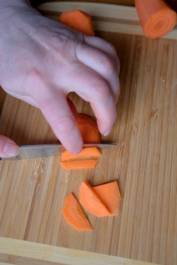 Yetenekli bir el, ahşap bir tahtanın üzerinde taze havuçları dilimler..