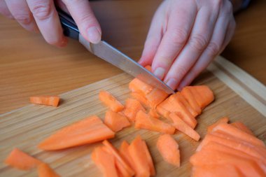 Eller ahşap kesme tahtasındaki canlı turuncu havuçları ustalıkla dilimliyor..