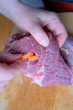 Eller ustalıkla taze ete havuç yerleştirir, aşçılık uzmanlığı gösterir..