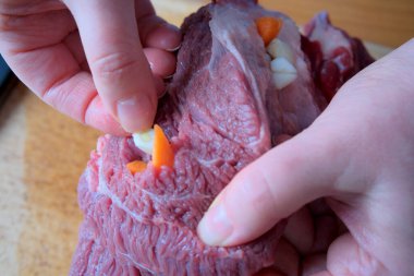 Eller ustalıkla baharat için çiğ ete sarımsak ve havuç yerleştirir..