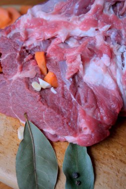 Taze et, sebze ve otlarla süslenmiş ahşap bir tahtanın üzerinde duruyor..