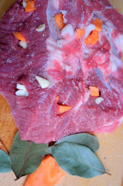 Sarımsak ve renkli sebzelerle süslenmiş çiğ bir et parçası pişmeyi bekliyor..