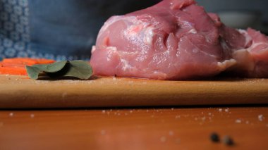 Taze domuz otların ve baharatların yanında ahşap bir kesim tahtasının üzerinde duruyor..