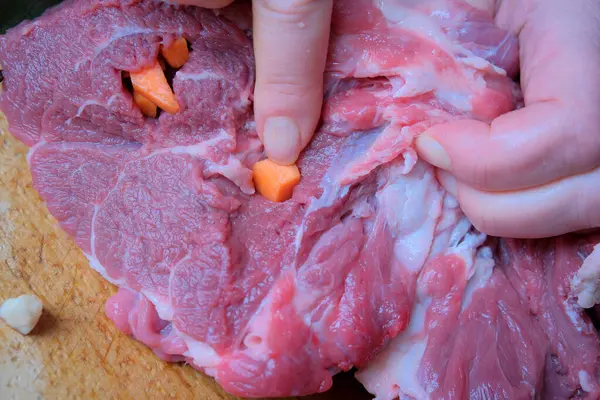 Birisi havuç parçalarını pişirmek için hazırlanmış etin içine yerleştirir..