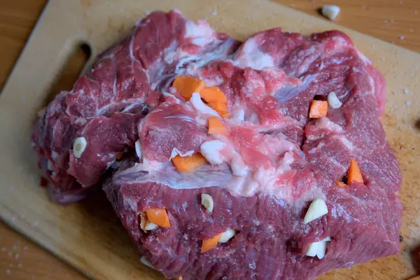 Kesme tahtasındaki çiğ et parçaları, sarımsak ve havuçla doldurulmuş..